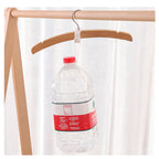 Clear plastic bottle with red label and cap hanging on a wooden hanger against a white curtain background.