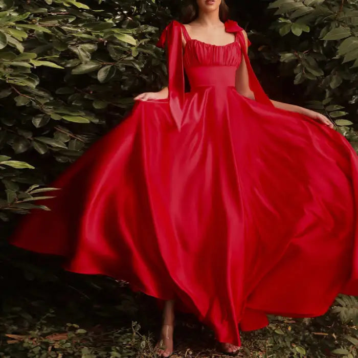 Model posing outdoors in a flowing red satin prom dress. The vibrant color and elegant design stand out against the greenery.