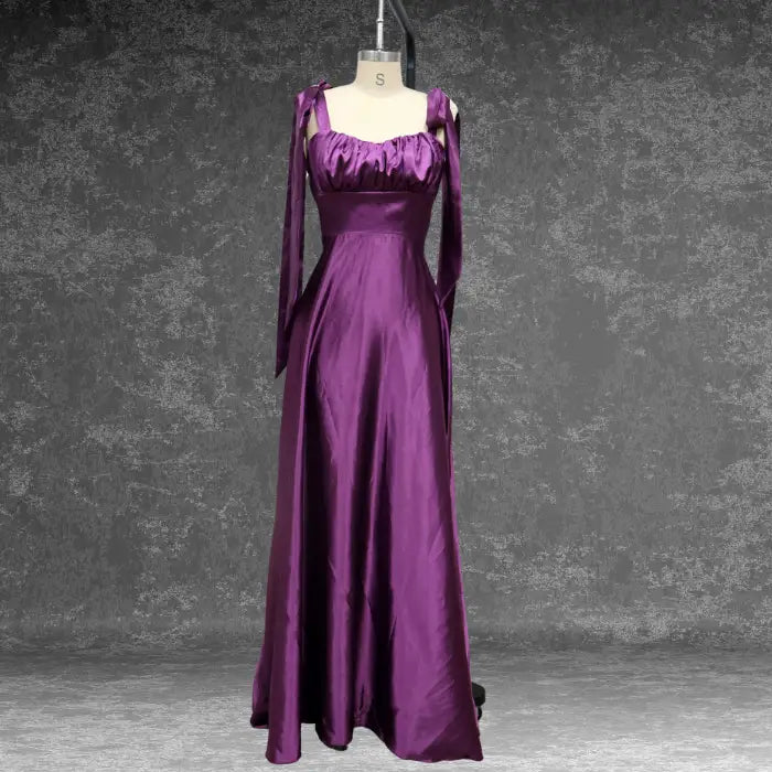 Model twirling in a glamorous purple satin prom dress by a window. The shiny fabric and full skirt make it ideal for evening.