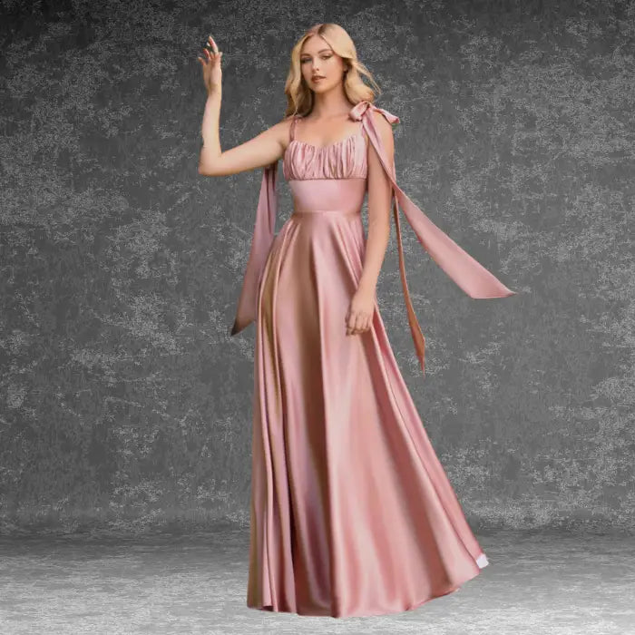 Model wearing a beautiful pink satin prom dress outdoors. Features delicate tie straps, ruched bust, and a graceful A-line skirt.