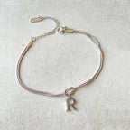 Silver bracelet with a letter 'R' charm on a light gray background