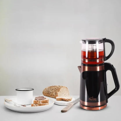 Electric teapot filled with tea on a kitchen table with a glass of tea and bread.