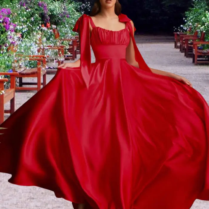 Model displays a vibrant red satin dress with full skirt outdoors. Features romantic tie straps, perfect formal evening wear.