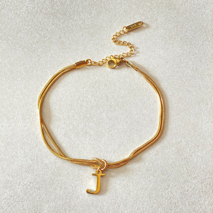 Gold bracelet with a letter 'J' charm on a light gray background