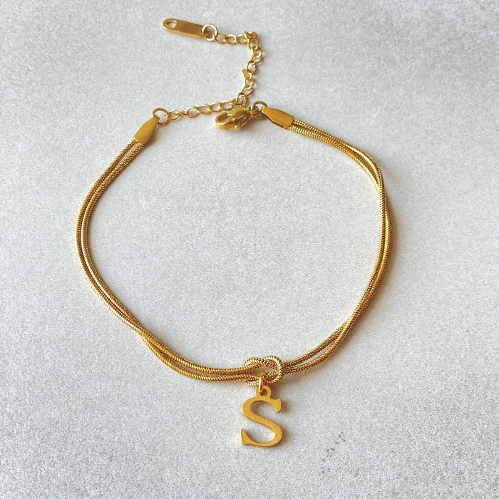 Gold bracelet with a 'S' charm on a light gray background