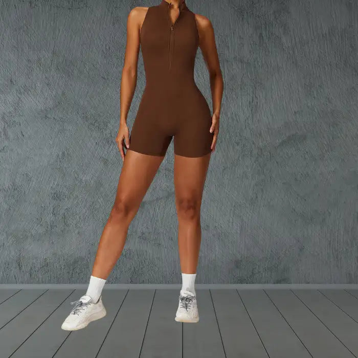 activewear jumpsuit in chocolate brown with front zipper closure and mock neck design styled with white sneakers against gray wall
