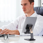 Adjustable phone stand holding a tablet at an office desk, offering ergonomic viewing height and stable support for work efficiency.