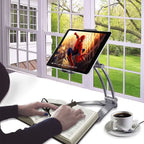 Adjustable tablet stand placed on a desk displaying a movie while a person reads, offering ergonomic hands-free device viewing for comfort