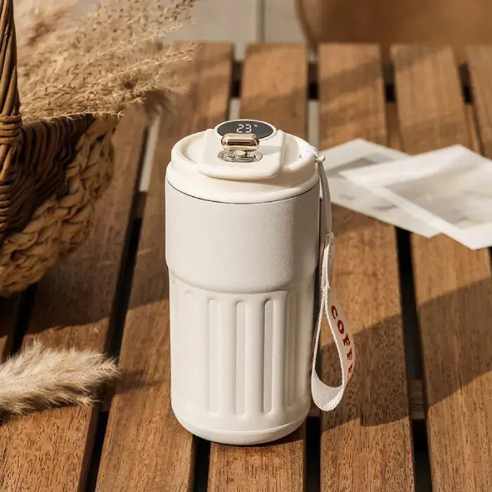 All-white smart coffee mug with digital display on wooden surface, emphasizing clean minimalist aesthetic