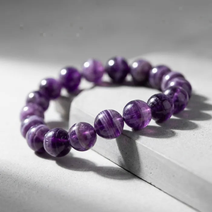 Amethyst jewelry bracelet with striped purple beads on stone surface, modern crystal accessory offering calming and elegant style