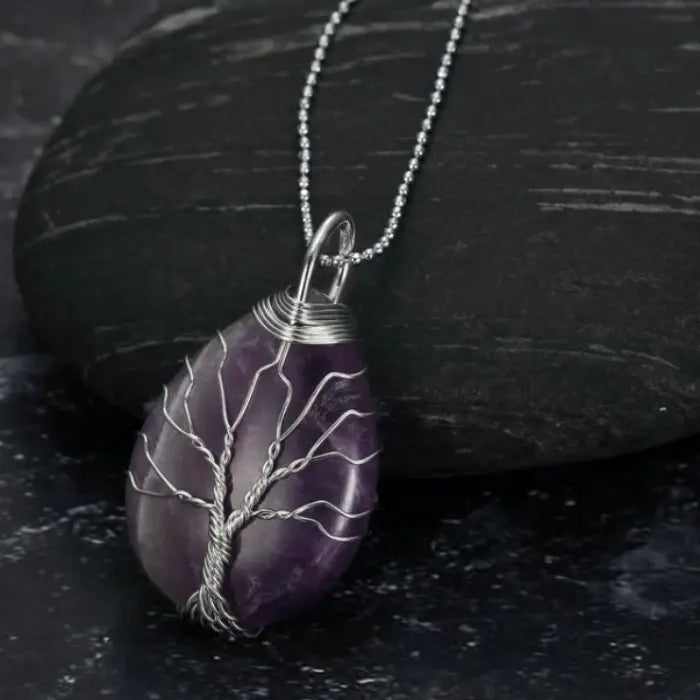 Amethyst teardrop gemstone pendant with silver wire tree of life design and silver chain on dark stone.