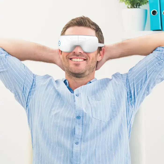 Smiling man relaxing with Anti-Wrinkle Eye Massager in a modern office setting.