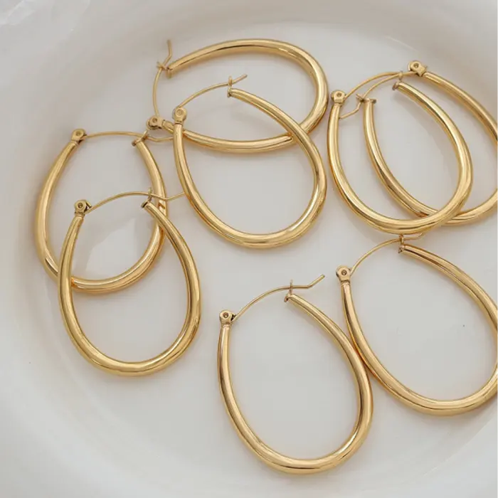 Multiple pairs of gold oval hoop earrings arranged on white plate