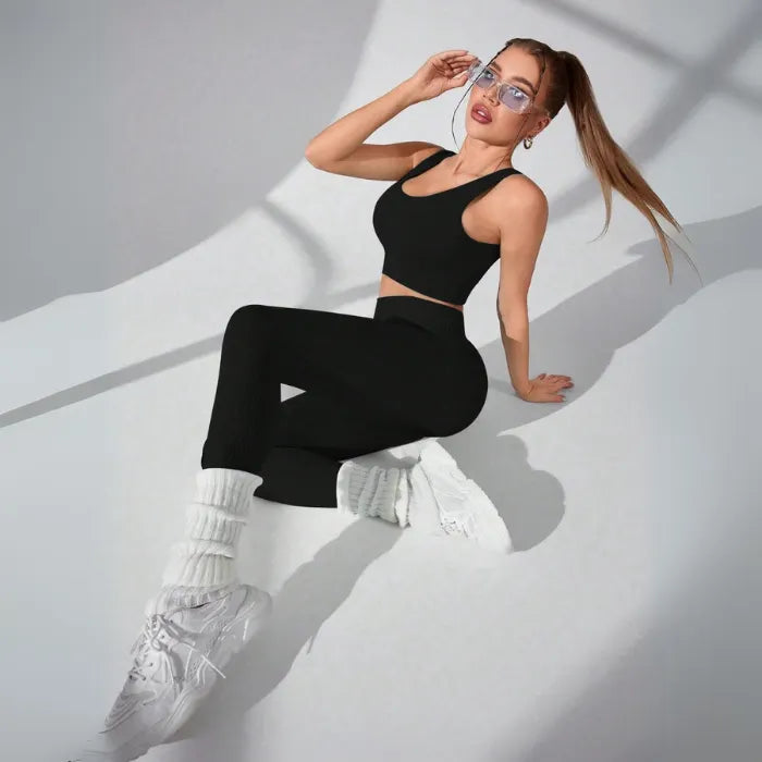 Athletic two-piece set in black ribbed fabric with white leg warmers and chunky sneakers, studio photography with dramatic shadows