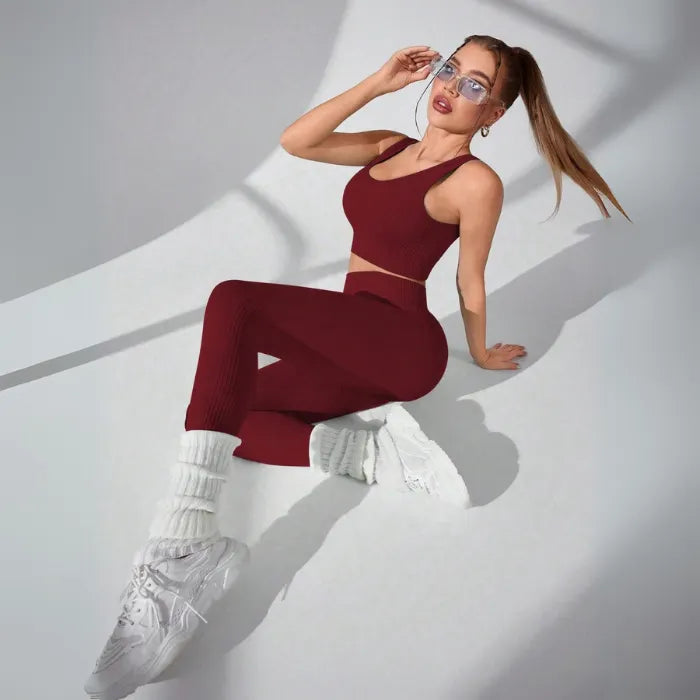 Athletic two-piece set in burgundy ribbed fabric with white leg warmers and chunky sneakers, studio photography with dramatic shadows