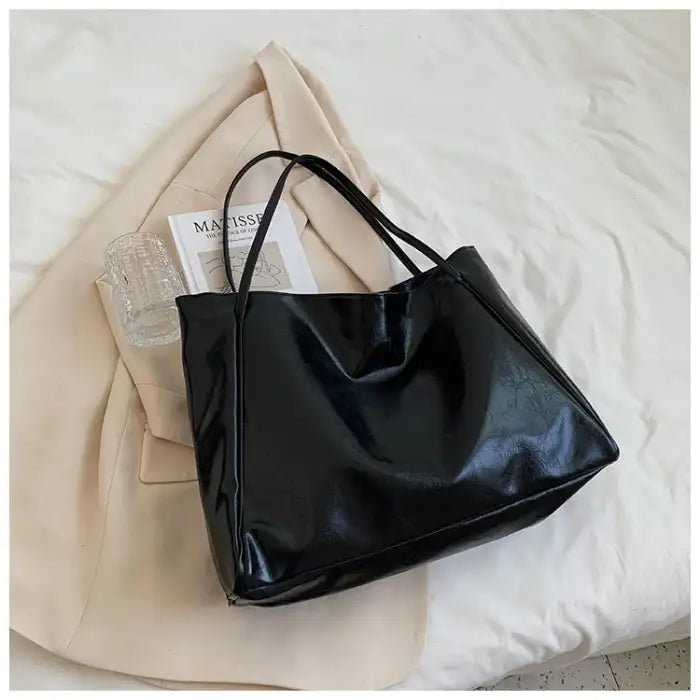 Autumn Shoulder bag in glossy black leather finish placed on cream blazer and book