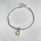Silver bracelet with a gold letter 'G' charm on a light gray background