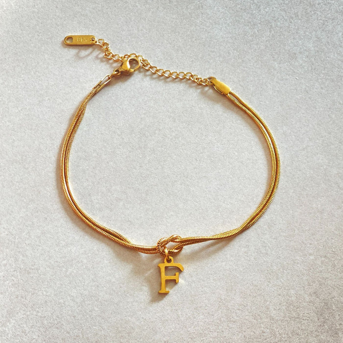 Gold bracelet with a 'F' charm on a light gray background