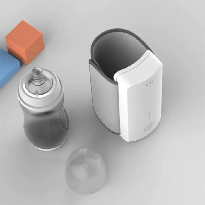 White bottle warmer with handle, baby bottle, and colorful toy blocks on gray surface, minimalist product arrangement