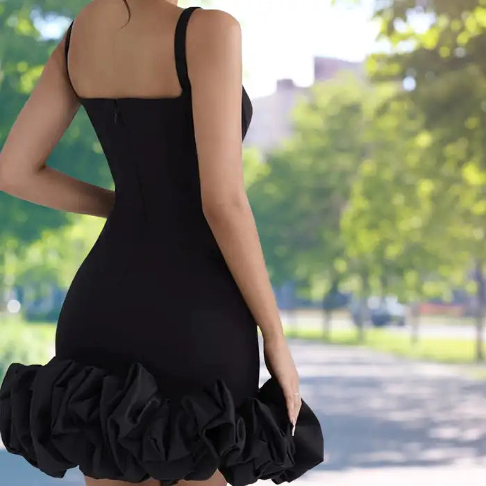 cocktail dress showcased from behind featuring fitted black silhouette with dramatic structured ruffle hem, photographed in park setting