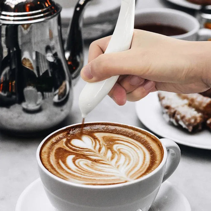 Hand creating intricate leaf pattern latte art in white ceramic cup using milk pouring tool