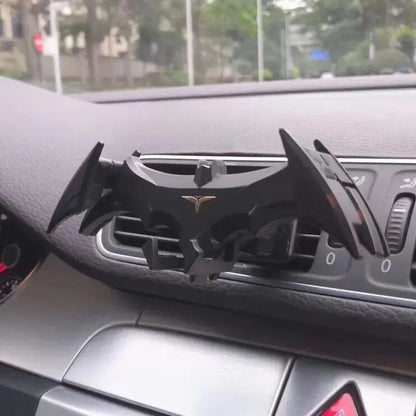 Black bat-shaped phone mount installed on car dashboard air vent, featuring distinctive wing design and metallic logo