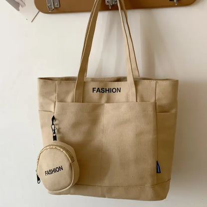 Beige canvas tote bag with detachable mini pouch, labeled "FASHION," hanging on a modern wall hook.