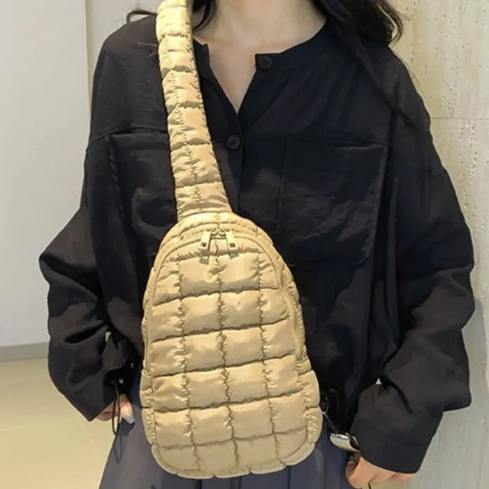 Beige puffer sling bag worn over black button-up shirt, person's torso visible, neutral-toned background