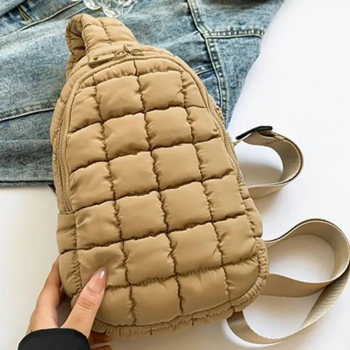 Beige puffy quilted crossbody bag with zipper closure and adjustable strap, displayed on denim jacket background