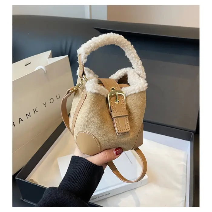  Beige suede bucket bag with sherpa trim being held over shopping bag and box packaging