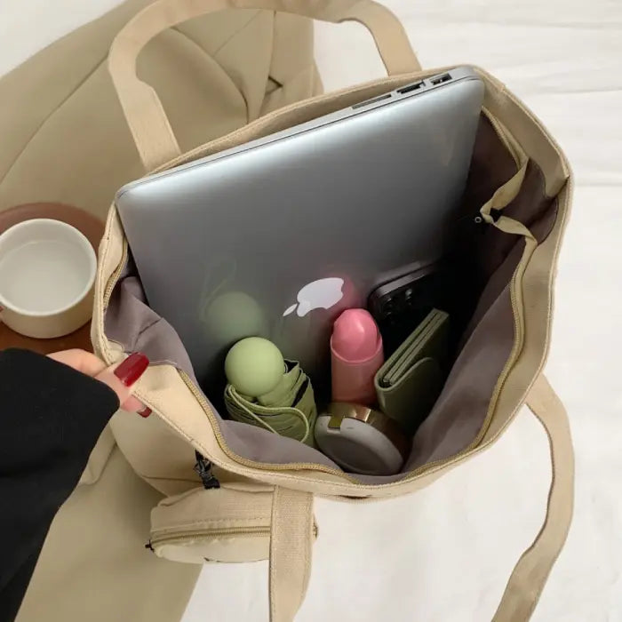 Beige tote bag filled with organized essentials, including a laptop, wallet, and other accessories.