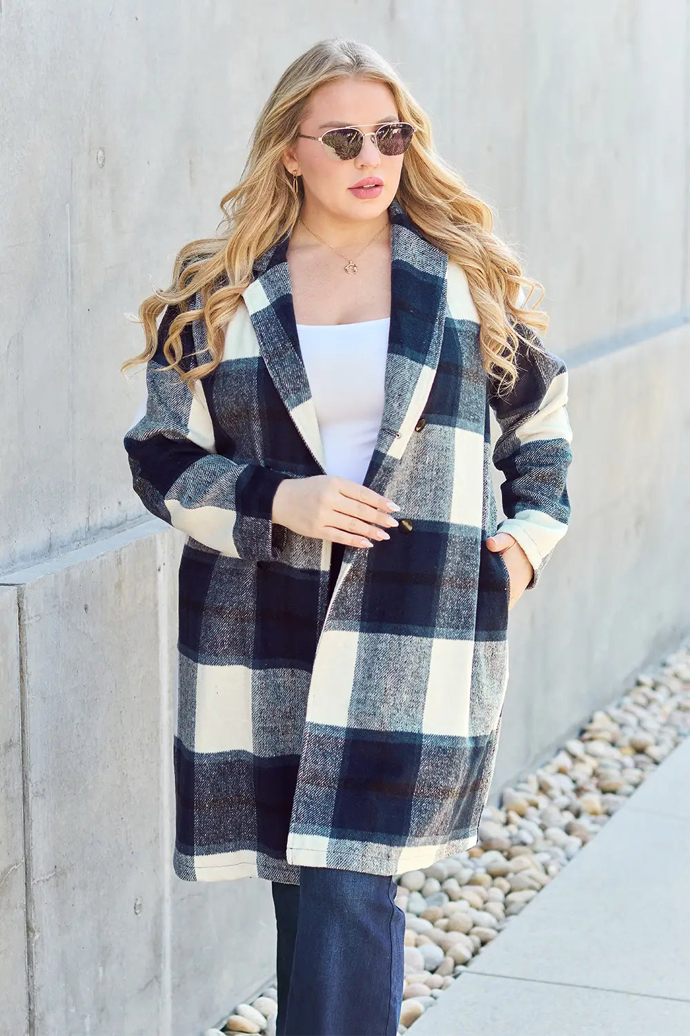 Woman in a black and white plaid wool coat styled with flared jeans, a white top, and sunglasses in an urban walkway.