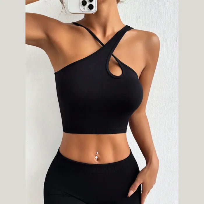 Side view of woman wearing black asymmetric crop top, showing toned arm and midriff with navel piercing