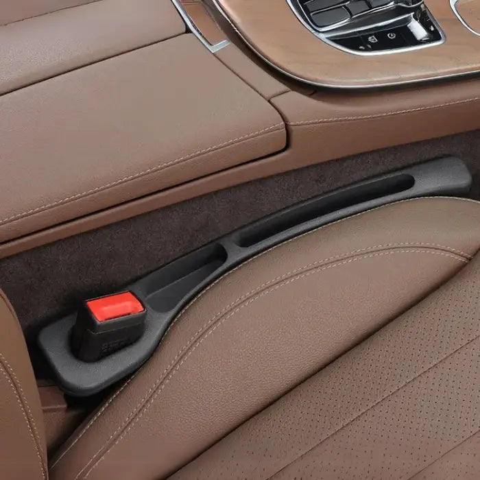 Black car seat gap filler installed in luxury vehicle with brown leather upholstery