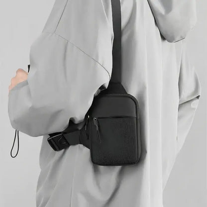 Black chest bag worn on side of light gray jacket, showcasing compact design and adjustable strap