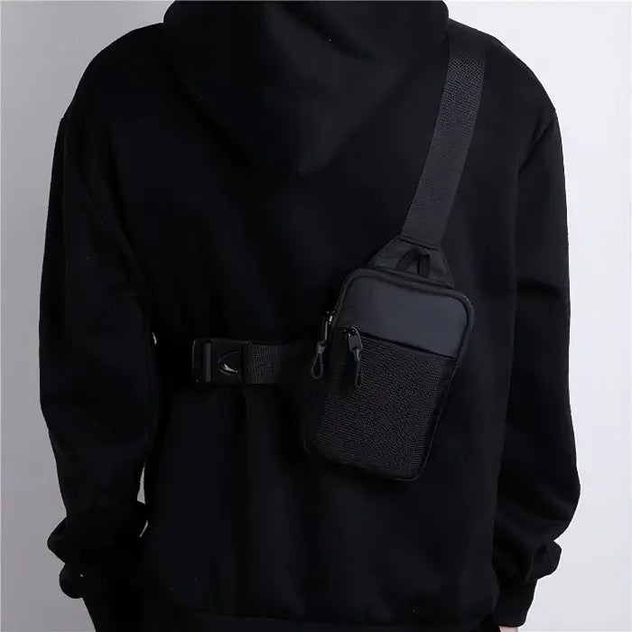 Person wearing black chest bag over black hoodie, demonstrating urban style and practical accessory use