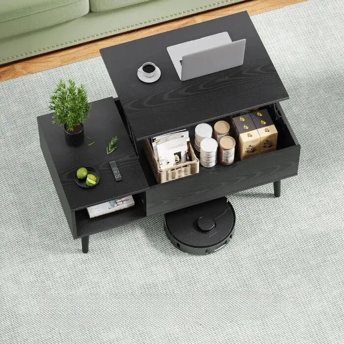 Modern black coffee table with lift-top revealing storage compartment, laptop, plant, and coffee cup on surface in living room setting