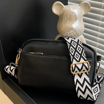 Black crossbody bag paired with a black-and-white chevron strap, offering timeless elegance and style.