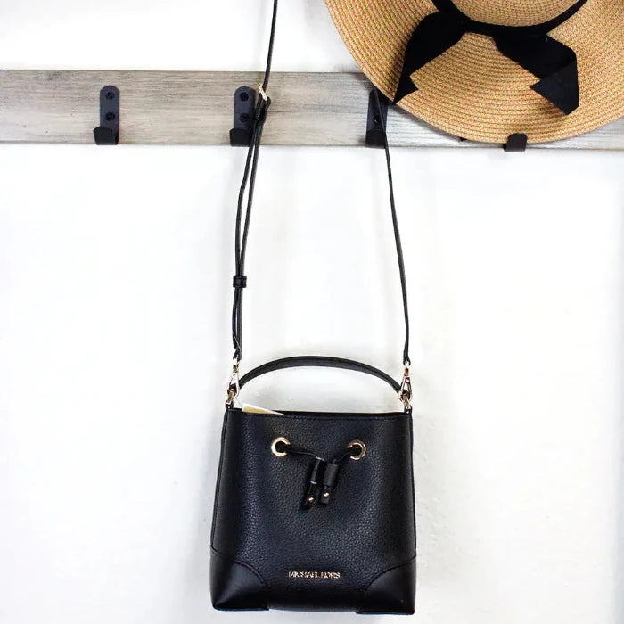 Black handbag hanging next to a straw hat on hooks, perfect for stylish summer outings.