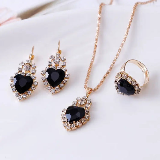 Black gemstone heart jewelry set with necklace, earrings, and ring surrounded by sparkling crystals.