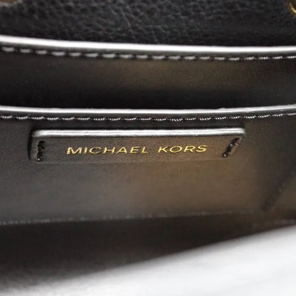 Close-up of Michael Kors brand logo on a black leather handbag, emphasizing luxury branding.