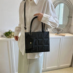 Person in white shirt and pants holding a black quilted handbag with geometric pattern and detachable shoulder strap