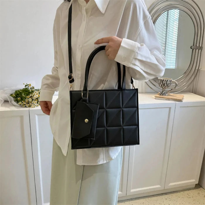 Person in white shirt and pants holding a black quilted handbag with geometric pattern and detachable shoulder strap