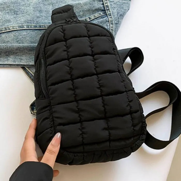 Black quilted sling bag with zipper closure and adjustable strap, displayed on denim jacket background