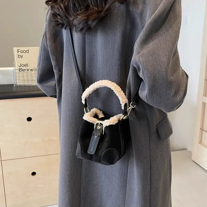 Black mini bucket bag with sherpa trim worn with grey long coat, showing crossbody styling