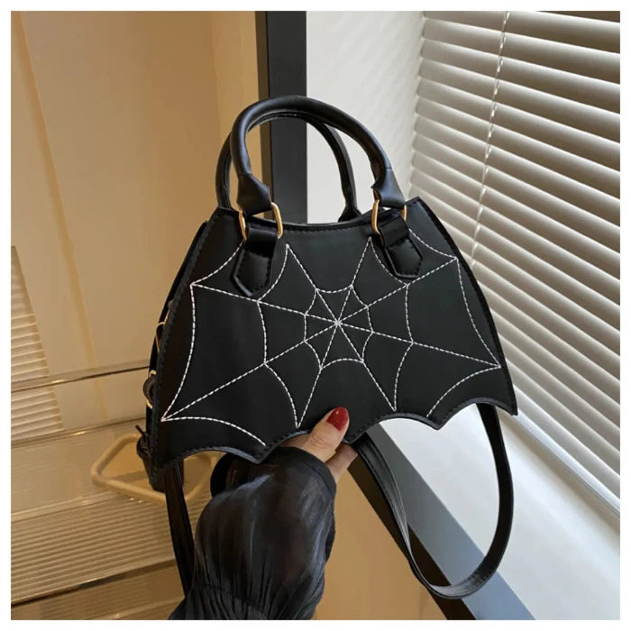 Black handbag with white spiderweb stitching, bat-wing shaped, held by hand with red nails against white blinds