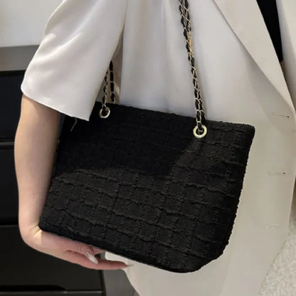 Person wearing white outfit carrying black textured bag with chain strap