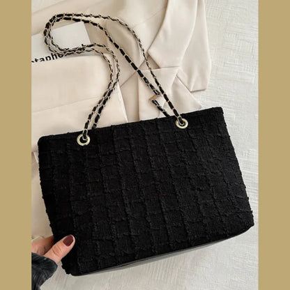 Black textured tote bag with woven chain handle on light background