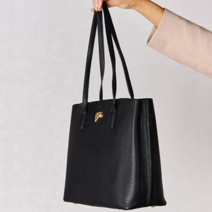 Close-up of a black leather tote bag held by hand, focusing on its gold emblem and textured leather surface