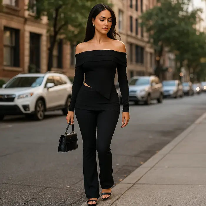 Black two piece outfit showcasing elegant off-shoulder design and side cutout detail while styled with handbag on urban city street